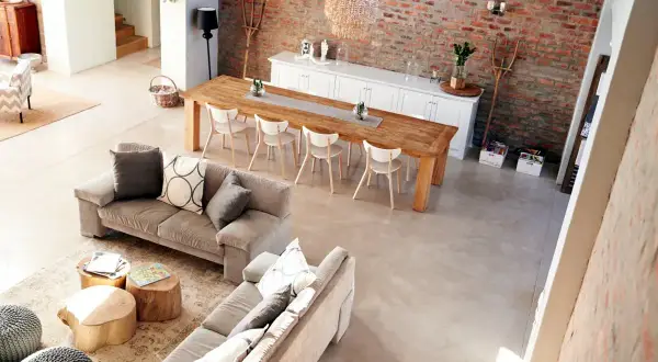 Nowoczesny salon w stylu rustykalnym z ceglaną ścianą, drewnianym stołem i wygodnymi sofami.