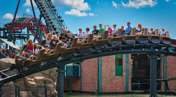 Energylandia otwarcie: wagoniki kolejki górskiej z pasażerami pędzą nad wodą, radość i emocje w parku rozrywki.