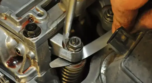 Mechanik reguluje zawory w silniku, używając śrubokręta i szczelinomierza.