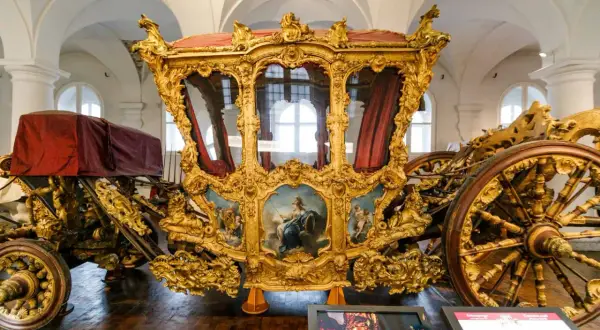 Prunkvolle Kutsche im Marstall Museum, vergoldet und mit Gemälden verziert, ein Zeugnis vergangener Pracht.