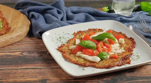 Eine köstliche low carb pizza mit Tomaten, Mozzarella und Basilikum auf einem weißen Teller.