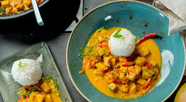 Ein köstlicher Thai Curry mit Tofu, Gemüse und Reis, garniert mit Frühlingszwiebeln und Chili.