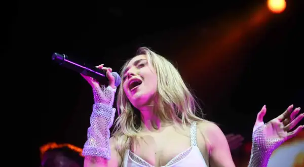 Ana Mena canta en Zaragoza, con un micrófono en la mano y guantes brillantes.