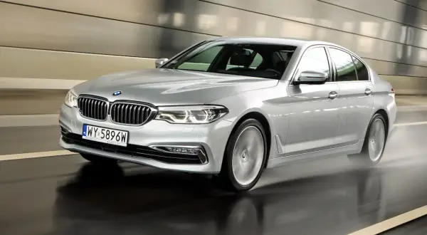 Srebrne BMW 520d xDrive pędzi po mokrej drodze w tunelu, rozpryskując wodę.