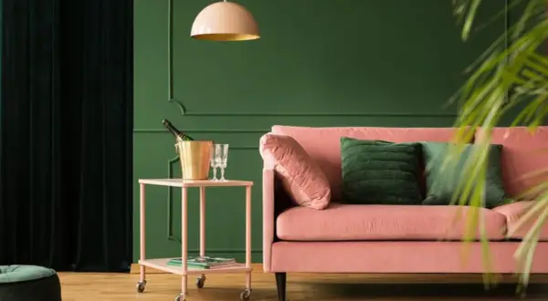 Różowa kanapa i złoty kubełek na szampana na stoliku. Wnętrze w odcieniach zieleni, gdzie kolory metali dodają elegancji.