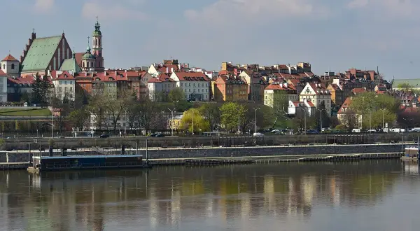 Widok na skarpa warszawska zapowiedzi, z kolorowymi kamieniczkami i zielenią, odbijającymi się w Wiśle.