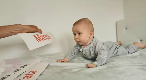 Zaciekawione niemowlę na brzuchu patrzy na kartkę z napisem "Mama". Obok leżą kartki "Tata" i "Tata jest silny".