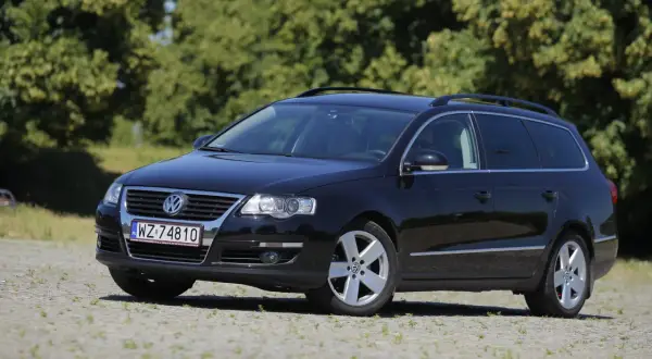 Czarny Volkswagen Passat kombi, model r36, zaparkowany na kamienistym podjeździe, z zielonymi drzewami w tle.