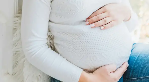 Gravid mage med händer som vilar på den. Kanske känner hon av ont i blygdbenet gravid.