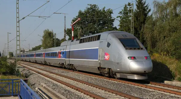 Srebrny pociąg TGV z niebieskimi pasami pędzi po torach, symbolizując niesamowitą prędkość.