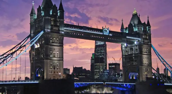 Wieczorny widok na Tower Bridge, jeden z najpiękniejszych zabytków w Londynie, z fioletowym niebem w tle.
