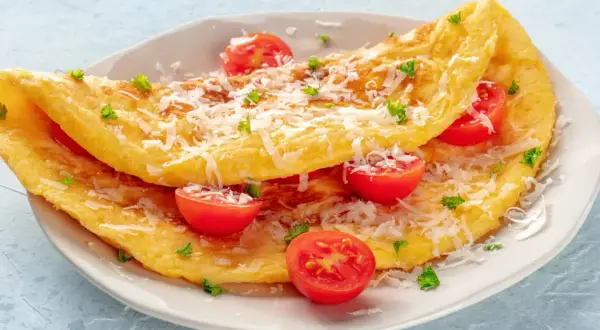 Puszysty omlet z serka wiejskiego, posypany parmezanem i udekorowany pomidorkami koktajlowymi i natką pietruszki.