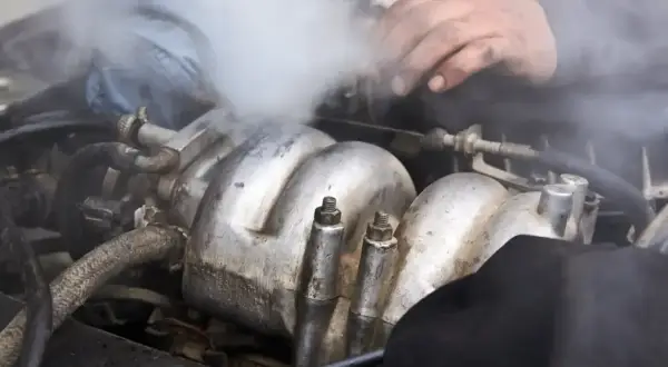 Mechanik próbuje naprawić silnik, z którego wydobywa się gęsty, biały dym.