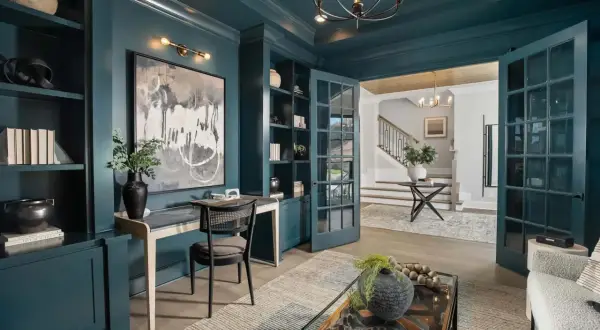 A study with a striking color drenching in deep teal. Built-in bookshelves, a desk, and French doors create a sophisticated workspace.