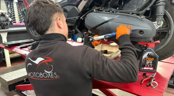 Mecánico con guantes naranjas realiza cambio de aceite a moto. Consulta el precio del cambio de aceite de moto y el aceite Motul.