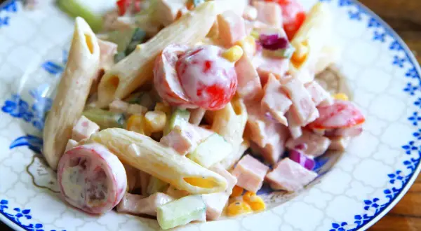 En krämig pastasallad med skinka, penne, körsbärstomater, gurka och majs. Perfekt för en snabb och god lunch.