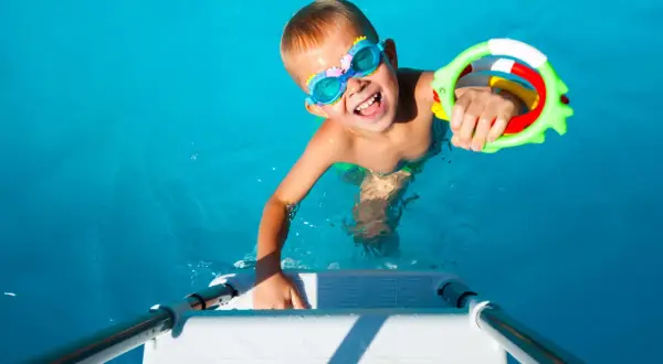Niño feliz con gafas de buceo y un juguete de agua, listo para juegos en la piscina.