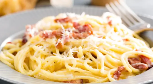 Spaghetti alla carbonara z boczkiem i parmezanem na szarym talerzu.