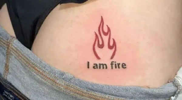 Płomień i napis "I am fire" na skórze, subtelny tatuaż na pośladku.