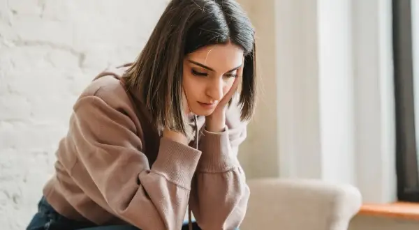 Una joven con las manos en la cara, con expresión de tristeza, parece reflexionar sobre qué es ser pesimista.