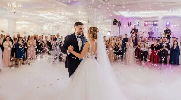 Para młoda tańczy na weselu, goście patrzą, zespół gra. W tle konfetti i dym. Piękny moment, ale czy wiesz o ukrytych kosztach wesela?