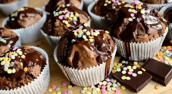 Czekoladowe muffiny polane lukrem i posypane kolorową posypką. Proste sposoby, jak dekorować muffiny, by wyglądały apetycznie.