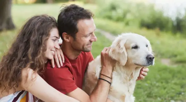 Un couple câlinant leur chien doré en plein air. Ils semblent réfléchir à comment faire garder son chien pour leurs prochaines vacances.