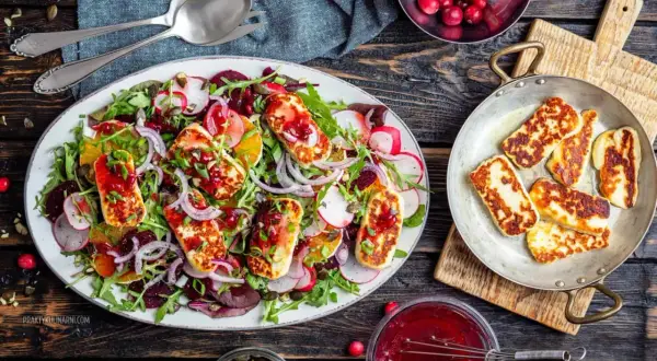 Kolorowa sałatka z grillowanym halloumi, burakami, pomarańczą i rukolą, polana sosem żurawinowym.