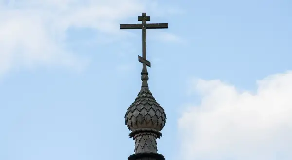 Drewniany krzyż na kopule cerkwi, symbol gruzińskiej religii prawosławnej, na tle błękitnego nieba z chmurami.