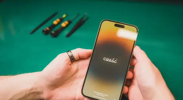 Dłonie trzymające iPhone'a z napisem "cześć" na ekranie, w tle narzędzia.