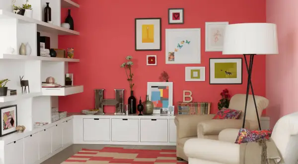 Wohnzimmer mit koralle farbener Wand, weißen Regalen, beigefarbenen Sesseln und einem Teppich mit roten und beigen Streifen.