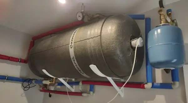 Duży bojler z rurami i niebieskim naczyniem przeponowym. Słychać bulgotanie w grzejniku, co może oznaczać potrzebę odpowietrzenia instalacji.