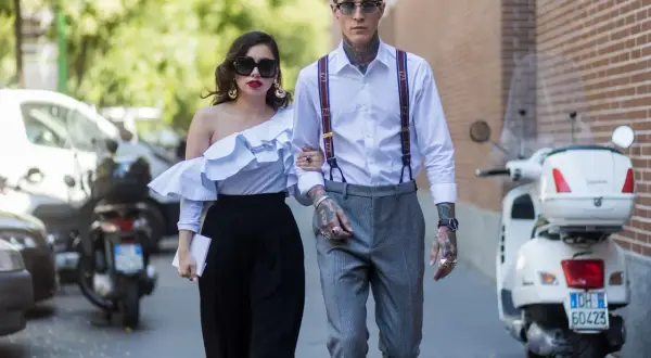 Pareja elegante pasea, él es un invitado boda hombre sin traje, con tirantes y tatuajes. Ella lleva un top blanco voluminoso.