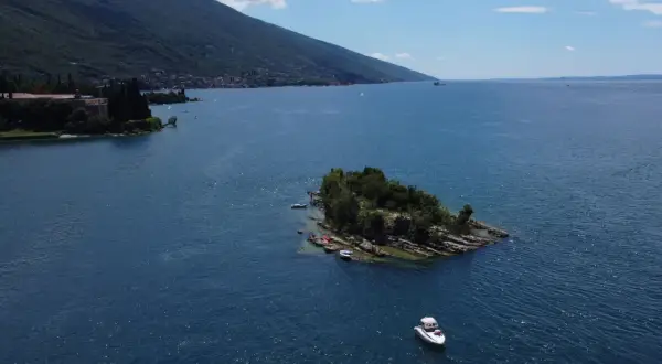 Un'isola verdeggiante nel Lago di Garda, con piccole imbarcazioni ormeggiate e una barca a motore che naviga nelle acque azzurre.