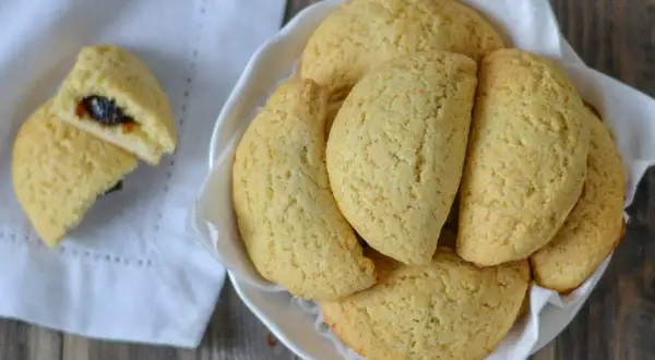 Dolci tipici bologna: biscotti dorati ripieni di marmellata, serviti in una ciotola bianca su un tovagliolo.