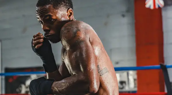 A boxer, sweat glistening, prepares for a head punch in the ring.