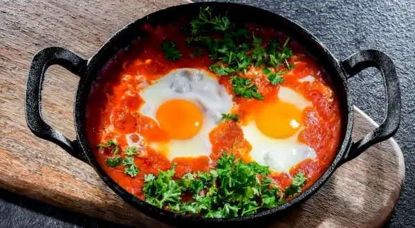 Herzhaftes Shakshuka-Rezept: Eier in würziger Tomatensoße, garniert mit frischer Petersilie, serviert in einer Gusseisenpfanne.