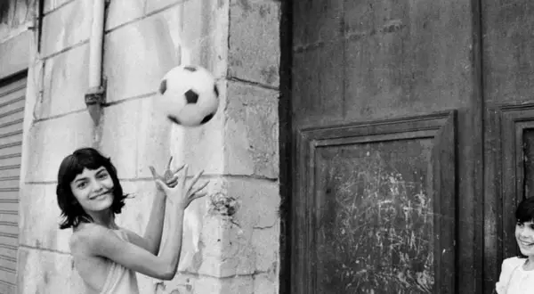 Letizia Battaglia giovane gioca con un pallone, un'immagine che cattura la spensieratezza dell'infanzia.
