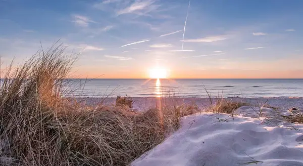 Sonnenuntergang am Strand, ein perfekter Urlaub in Deutschland. Dünen mit Gräsern und Sand, das Meer glitzert.