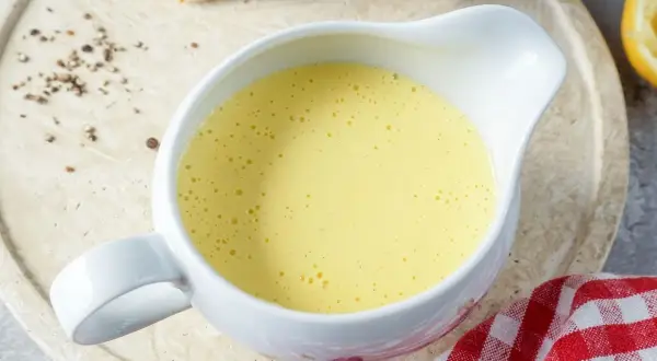 Cremige Sauce Hollandaise in einer Sauciere, daneben Spargel und Zitronenspalte. Perfekt für ein Frühlingsgericht.