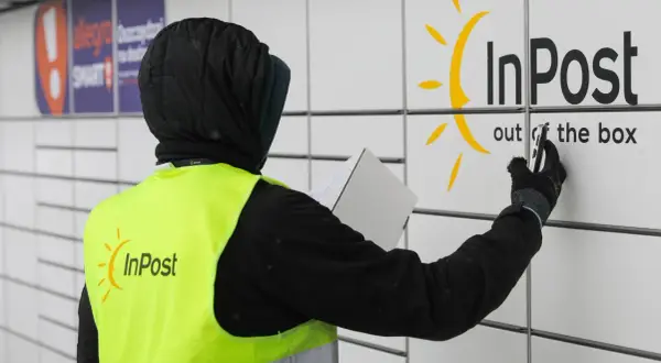 Pracownik w kamizelce InPost z paczką przy paczkomacie. Czy muszę naklejać etykietę InPost? Nie, wystarczy kod nadany przez system.