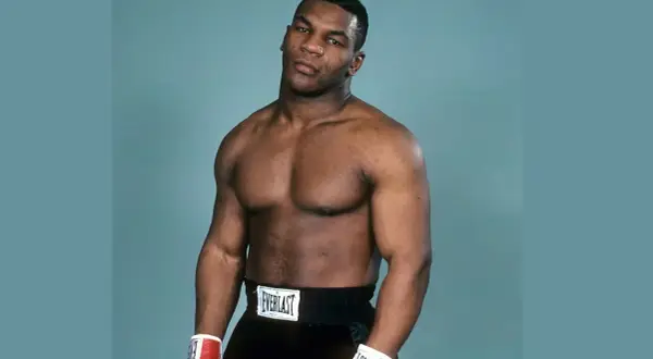 Mike Tyson's powerful physique is on full display, showcasing his legendary mike tyson abs and muscular chest. He wears boxing shorts and gloves.