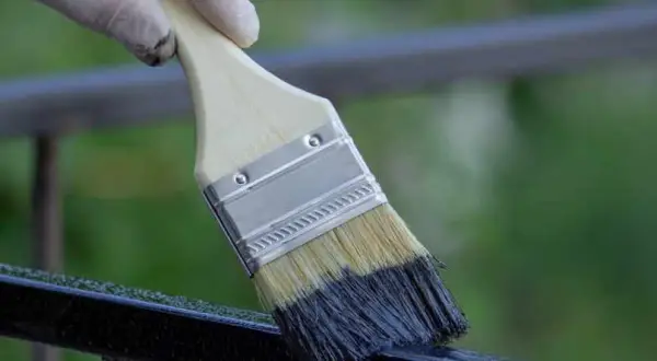 Mano guantata che inizia a verniciare ringhiera con pennello nero.