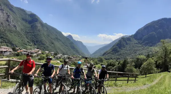 Grupa rowerzystów na malowniczym szlaku stu jezior, podziwiająca górską panoramę i urokliwą wioskę.