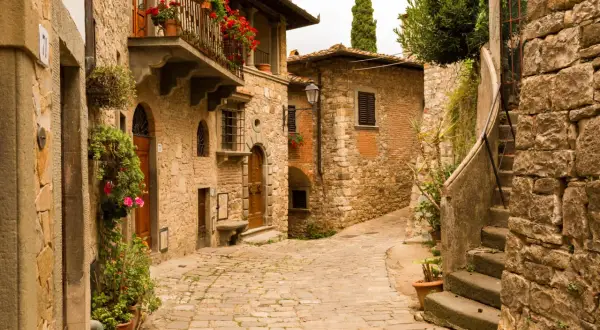 Un vicolo acciottolato tra antichi borghi toscani poco conosciuti, con case in pietra, balconi fioriti e un'atmosfera senza tempo.