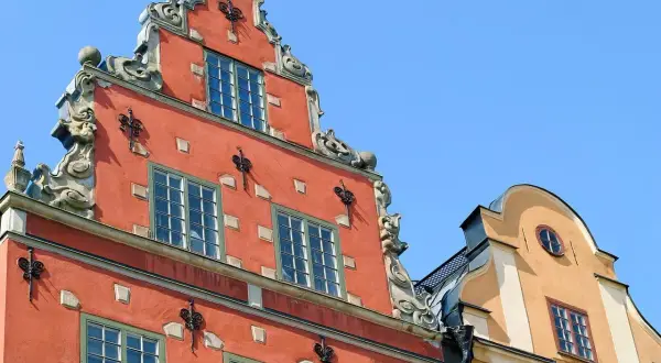 Fasaderna på ett gammalt hus i Stockholm, som en gång kan ha varit ett slott eller värdshus, med detaljerad utsmyckning och röda och gula färger mot en blå himmel.