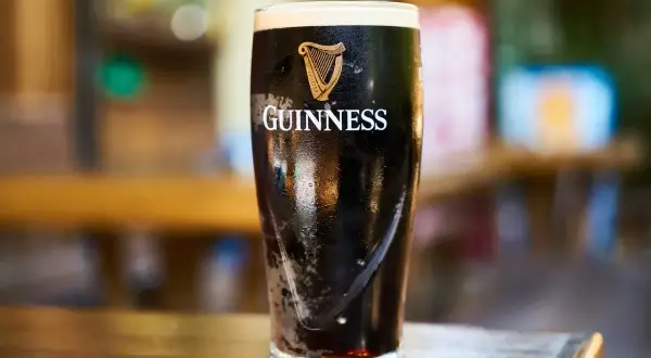Szklanka z ciemnym piwem słodowym Guinness, z charakterystycznym logo harfy i napisem. Piana tworzy grubą warstwę.