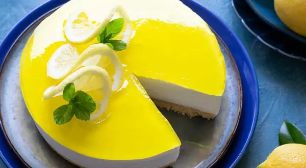 Cheesecake lime lucido con decorazioni di limone e menta, una fetta è stata tolta.