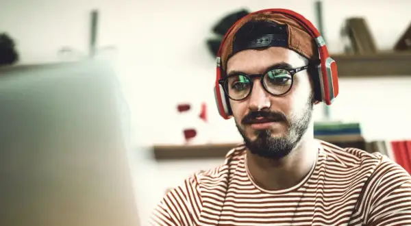 Junger Mann mit Kopfhörern und Brille lernt für seinen berufsbegleitenden Master in Stuttgart.