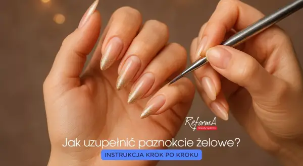 Dłonie z długimi, migdałowymi paznokciami pokrytymi złotym, miękkim żelem. Pędzelek do zdobień zbliża się do jednego z paznokci.
